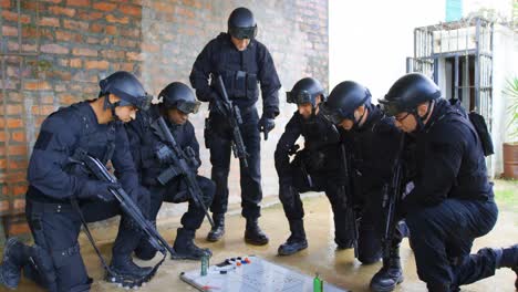 Side-view-of-mixed-race-military-soldiers-with-rifles-planning-and-crouching-on-floor-at-base-4k