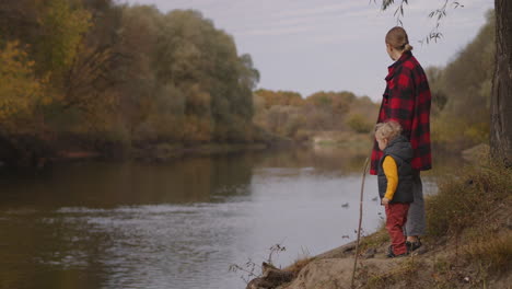 little-child-boy-with-his-mother-are-standing-on-shore-of-picturesque-forest-river-and-enjoying-autumn-nature-trip-in-forest-at-weekend-family-rest-at-vacation
