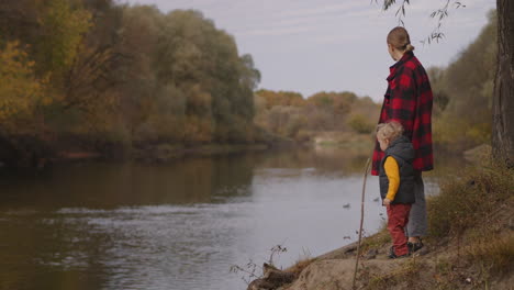 little child boy with his mother are standing on shore of picturesque forest river and enjoying autumn nature trip in forest at weekend family rest at vacation