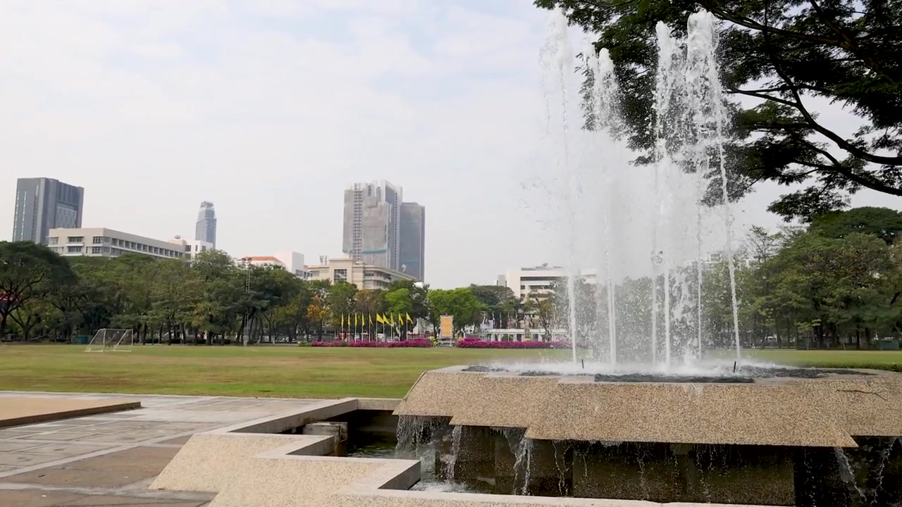 Plano general estático de una fuente de piedra escalonada con chorros de agua, con el telón de fondo del horizonte de una ciudad.