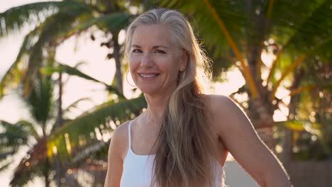 Pretty-mature-woman-looks-off-screen-to-left-and-then-to-the-camera-as-sun-flares-behind-her-in-a-tropical-palm-tree