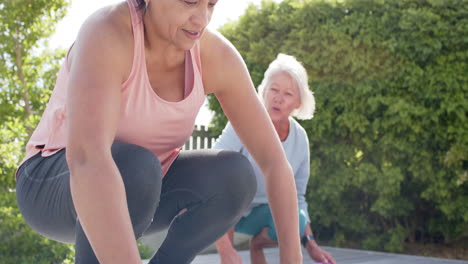 Two-happy-diverse-senior-women-rolling-up-mats-and-discussing-in-sunny-garden,-slow-motion