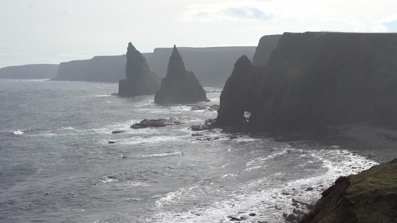 Wild beauty of the Scottish coast with sight of Duncansby Stacks rising majestically from the sea, adorned with an abundance of nesting birds that gracefully soar through the air