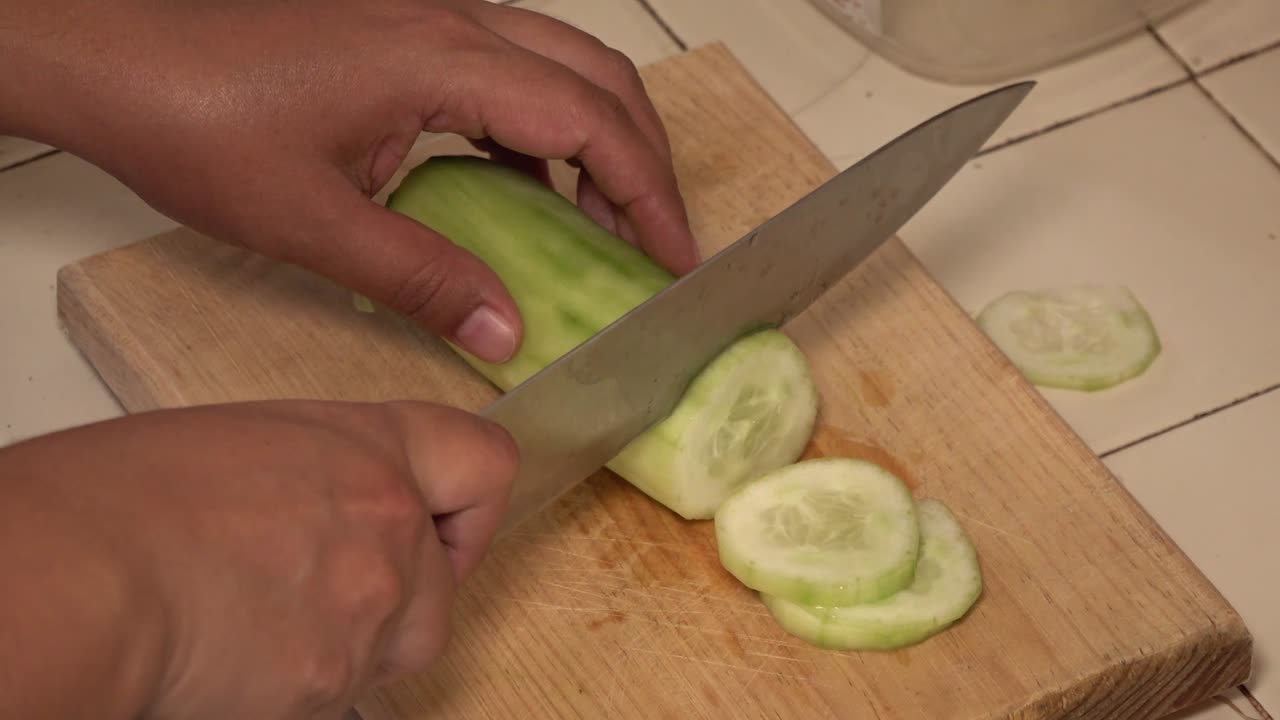 manos cortando un pepino en una tabla de cortar