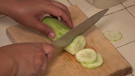 hands slicing a cucumber on a cutting board