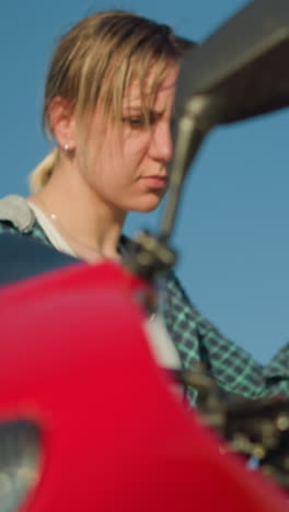 se ve a una mujer joven preparándose para montar una poderosa motocicleta roja, agarrando la palanca del embrague con atención