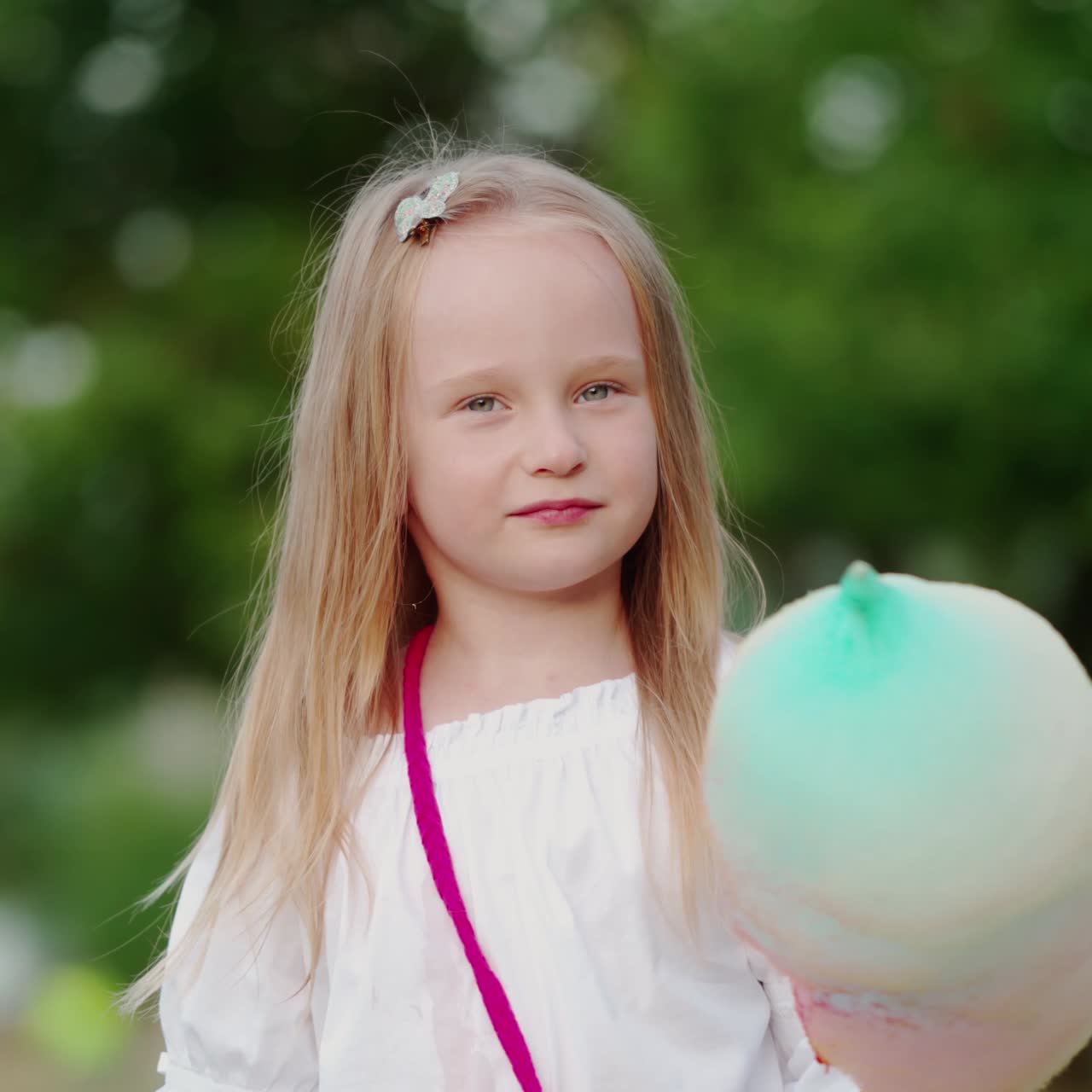 Little girl eating candyfloss in the park. Happy child holding sweet colorful cotton candy and eat outdoors.