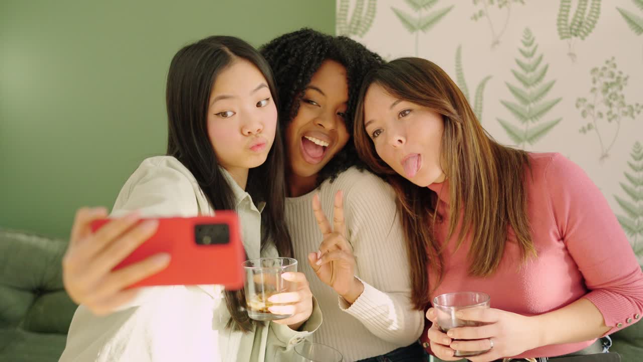 Multiracial women pulling funny faces while taking a selfie indoors
