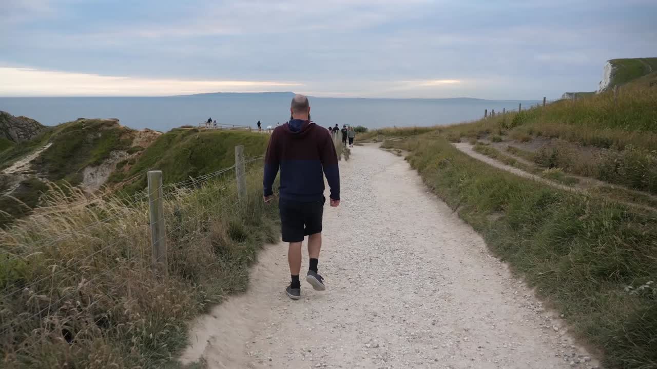 A man walking down a mountainous pathway towards the sea