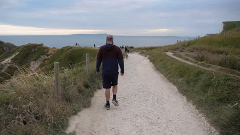 a man walking down a mountainous pathway towards the sea