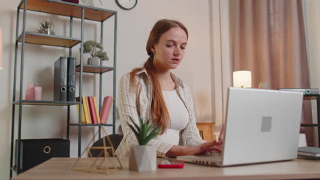 Young-woman-girl-using-laptop-computer-sitting-at-table-working,-online-shopping-from-home-office