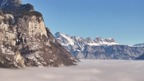 aerial shot of snow-covered mountains towering above a sea of fog in the amden and arvenbüel region of switzerland, showcasing the beauty of the alpine landscape.