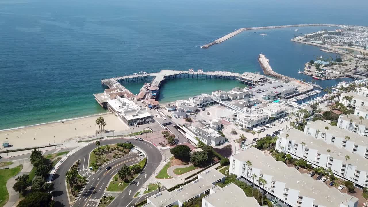 Kaliforniya, Redondo Beach Limanı’nın tekneler, yolcu gemisi rıhtımları, kavisli iskele, marina suları ve Pasifik Okyanusu kıyısındaki çevredeki kıyı binalarıyla berrak bir günde çekilmiş havadan görünümü