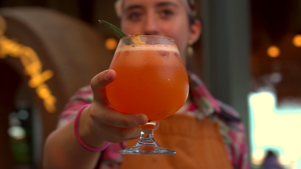 Barista mixologist donna latina mostra un drink fresco in bicchiere, cocktail agrumato con arancia e limone, in un ristorante-cantina sulla spiaggia in Messico/Caraibi.