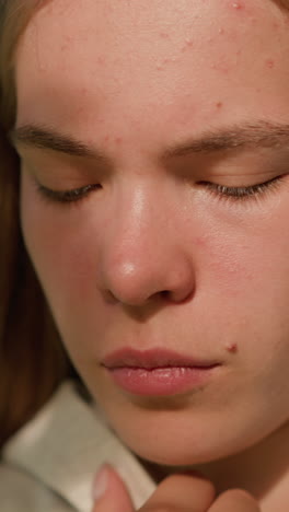close-up of young woman in deep thought holding hood collar, face softly illuminated by sunlight filtering through leaves, with background greenery blurred
