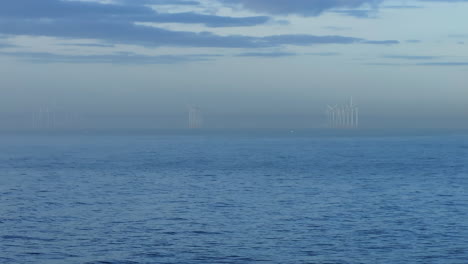 establishing drone shot over sea with wind turbine farm in the distance