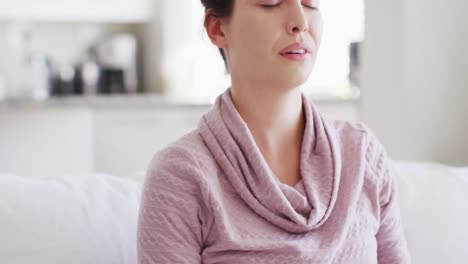 happy caucasian woman sitting on couch and meditating in living room