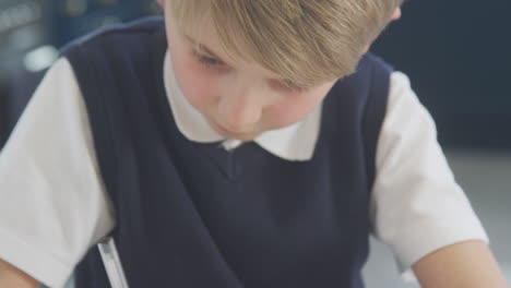 boy at home wearing school uniform doing maths homework on kitchen counter