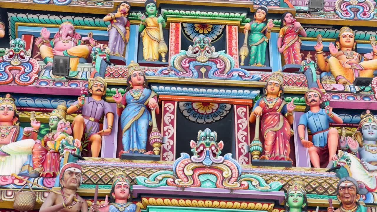Camera slowly pans down the vibrant, intricately detailed facade of a Hindu temple in Singapore, highlighting ornate statues and vivid architectural elements in daylight