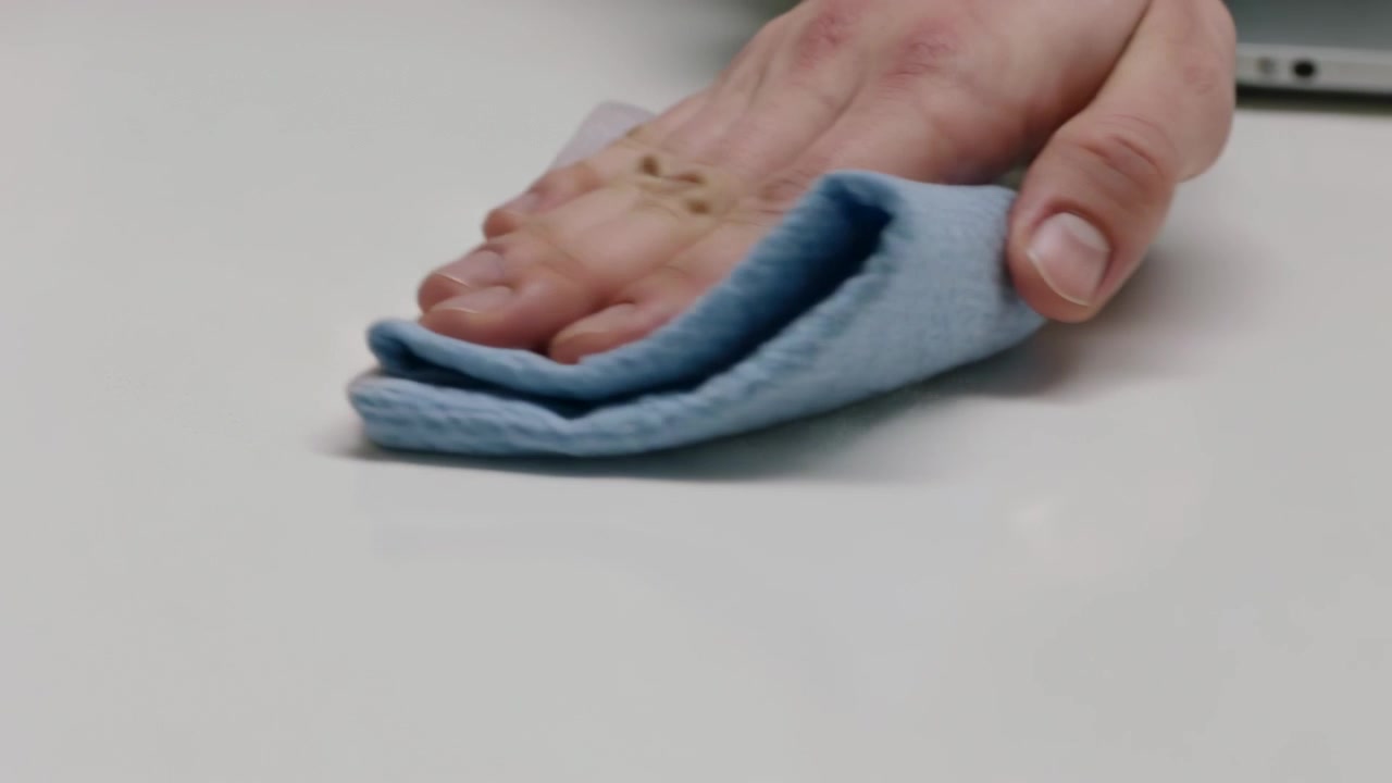 Přitlačování složené látky, utírání rukama, opětovné skládání přes bílý stůl pro čištění, tmavý rukáv, notebook.