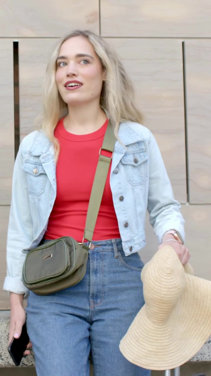 Video vertical: Mujer con blusa roja, sombrero de paja y teléfono, entrando por la izquierda en una pared beige, escaneando.