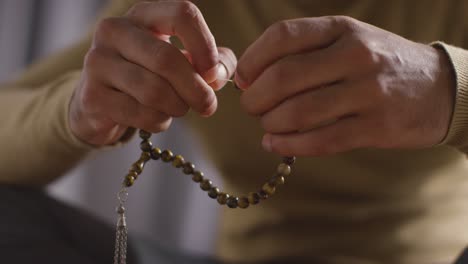 Close-Up-Of-Muslim-Man-Praying-Holding-Prayer-Beads-Sitting-On-Floor-At-Home-1