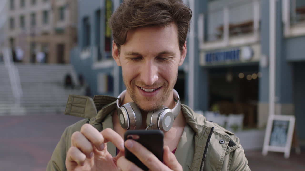 retrato de un apuesto joven caucásico usando un teléfono inteligente navegando en una aplicación móvil enviando mensajes de texto fondo urbano