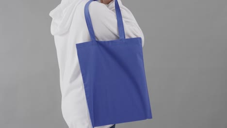 caucasian woman wearing white hoodie holding blue bag on grey background, copy space, slow motion