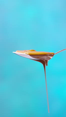 video vertical de chocolate derretido goteando de una cuchara desbordante contra un fondo de color azul con espacio de copia 1