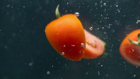 trozos de tomate cortado bajo el agua con burbujas de aire y en cámara lenta. productos vegetarianos frescos y jugosos ingredientes de ensalada