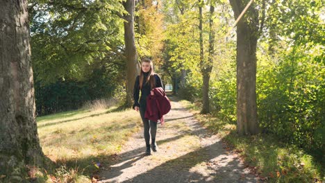 Woman-with-long-hair-walks-along-an-avenue-of-trees-on-a-sunny-autumn-day-in-slow-motion