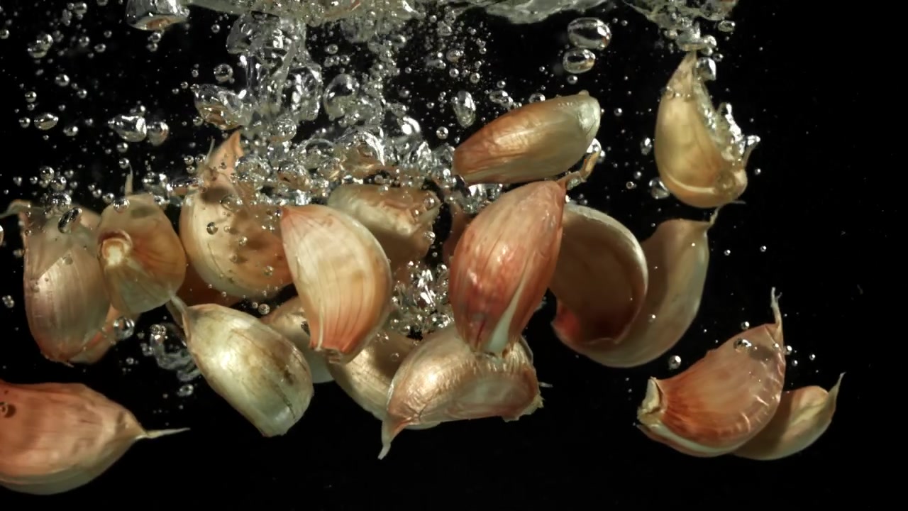 Knoblauchzehen fallen mit Blasen ins Wasser auf schwarzem Hintergrund