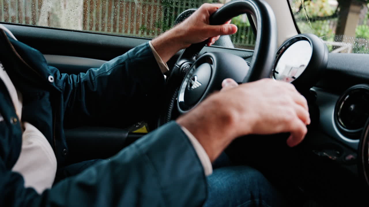 Close up of a man's hands on a steering wheel, driving a car on the road in the rain