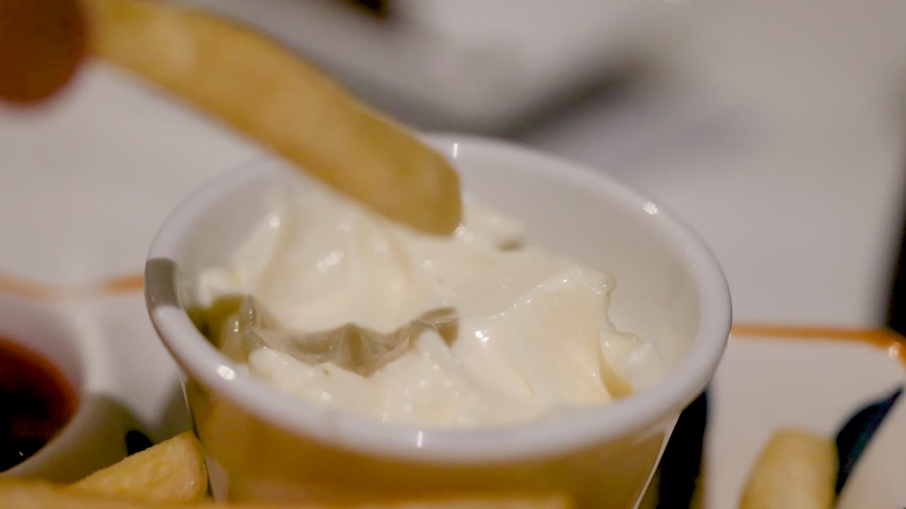 Una sequenza che mostra una patatina fritta che viene intinta in una tazza di maionese cremosa, evidenziando un semplice momento culinario.