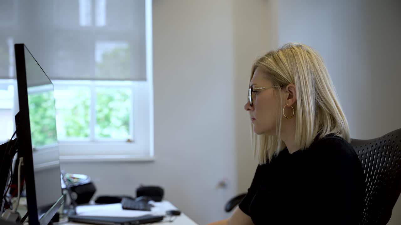 En profesjonell setting med en blond kvinne fokusert på arbeidet sitt ved et databord på et godt opplyst kontor