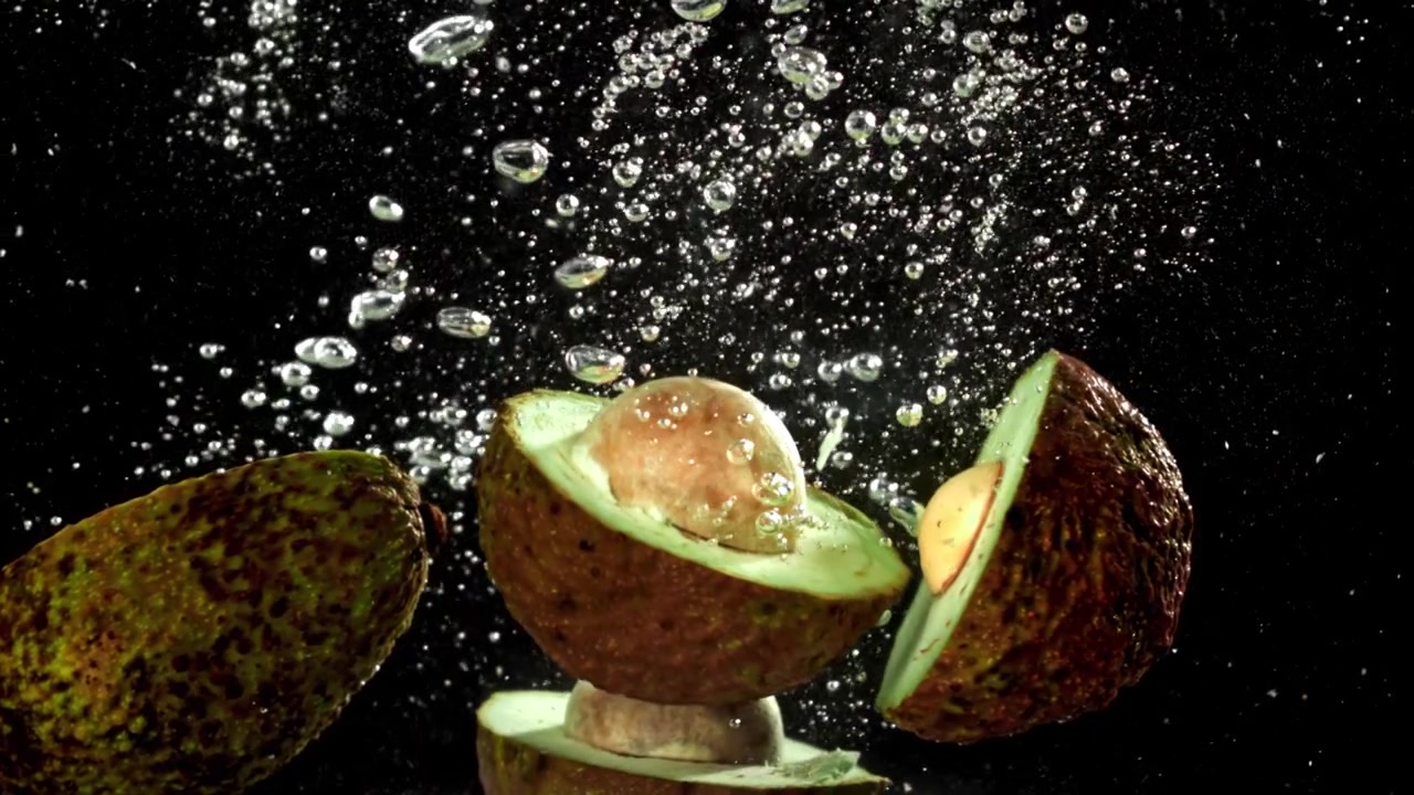 Avocadi freschi che cadono nell'acqua con bolle al rallentatore