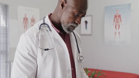 Portrait-of-african-american-male-doctor-wearing-lab-coat-and-stethoscope,-using-tablet,-slow-motion