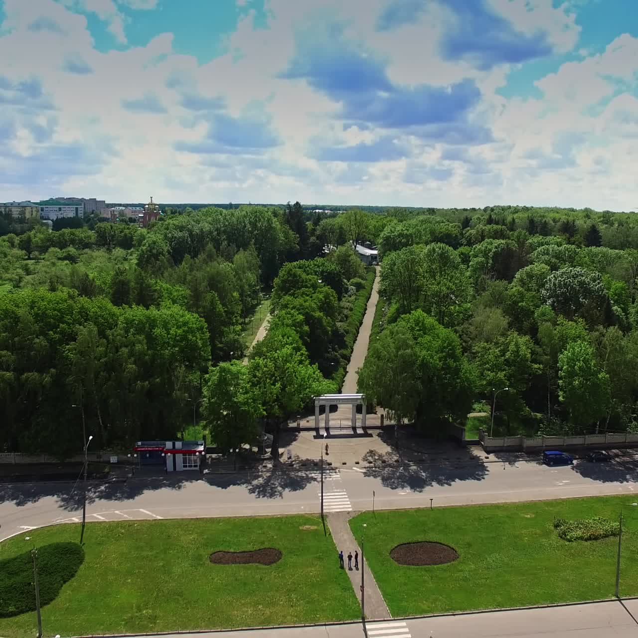Entrance of the green city park with long road in the middle. Drone footage rising over the crossroads on sunny day