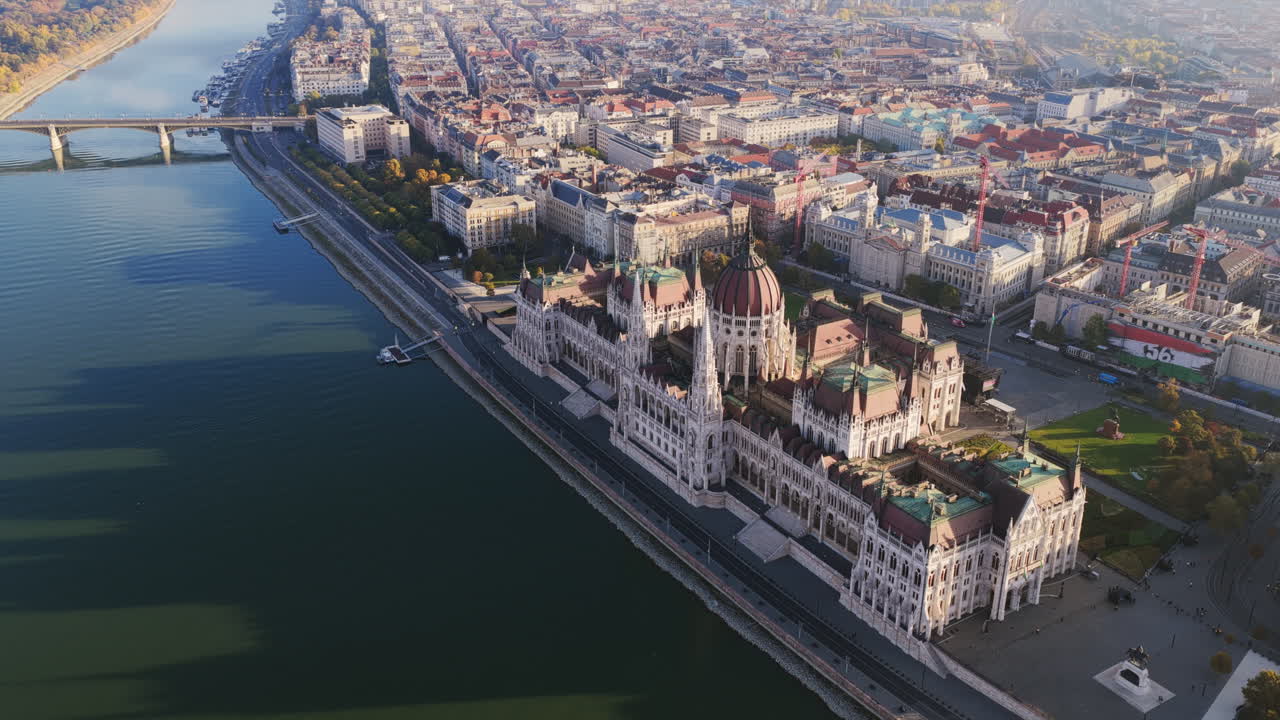 Sunlit aerial view of Budapest’s Parliament overlooking the Danube, framed by riverside streets and the bridge to Margaret Island