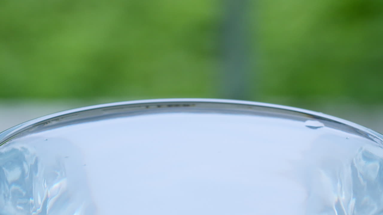 물방울은 파동과 표면 긴장을 일으키며 투명한 유리 용기에서 물의 움직임을 초래합니다.