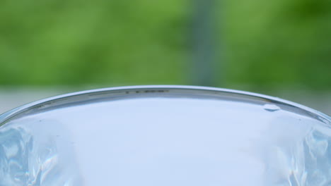 wassertropfen erzeugen wellen und oberflächenspannung, was zu einer bewegung des wassers in einem durchsichtigen glasbehälter führt