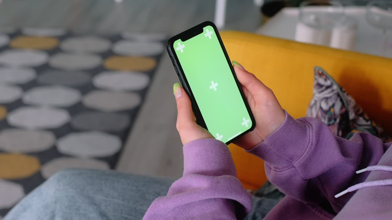 Young woman sitting on armchair at home and uses smartphone with green screen Mock-up. 4k