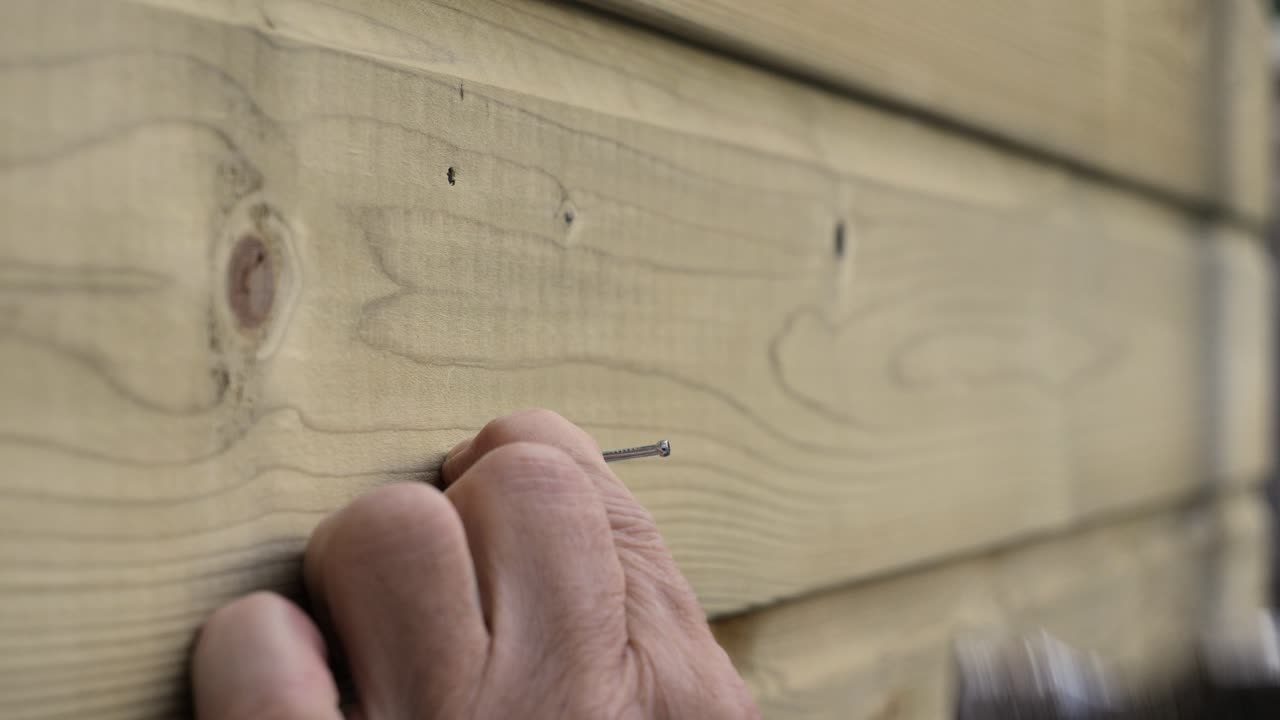 Carpenter's hands drive nails into wooden boards, close‑up DIY construction footage.