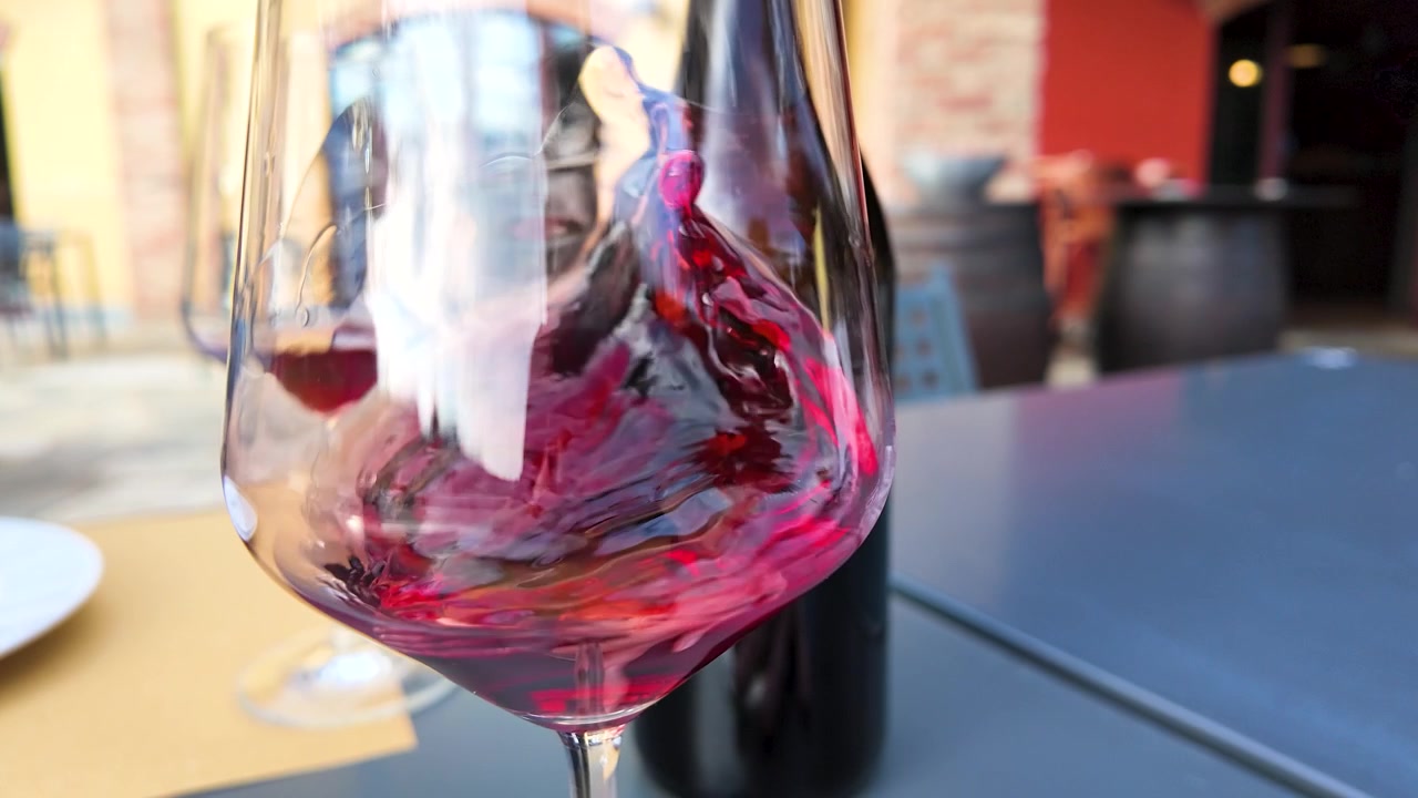 Primo piano di vino rosso che volteggia all'interno di un bicchiere su un tavolo da pranzo all'aperto.