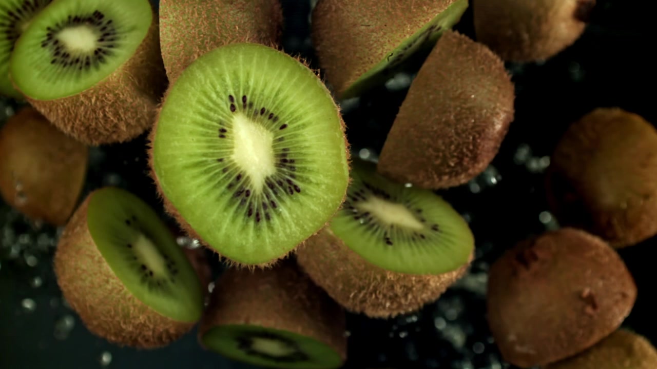Rodajas de kiwi fresco y kiwis enteros cayendo con gotas de agua a cámara lenta
