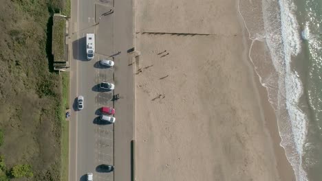 vista aérea de arriba hacia abajo de una carretera muy transitada junto a una playa de arena y olas turbias del océano