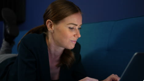 una chica atractiva tendida en un sofá por la noche usando una laptop