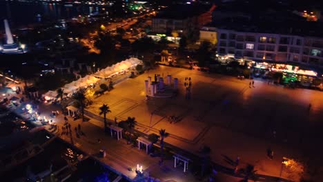 aerial shot circulating well lit portuary city with palm trees, people walking and boats