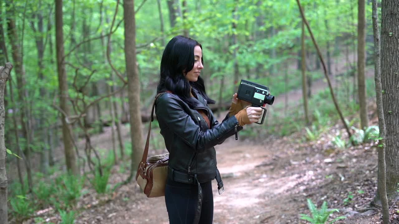 Ung attraktiv kvinde betaget af et gammeldags filmkamera i skoven om dagen - koncept: minder, gammel, retro, hobby, turist, prøver nye ting - medium gimbal-optagelse i slow motion