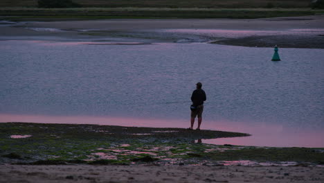 fisherman fishing at sunset on estuary at low tide